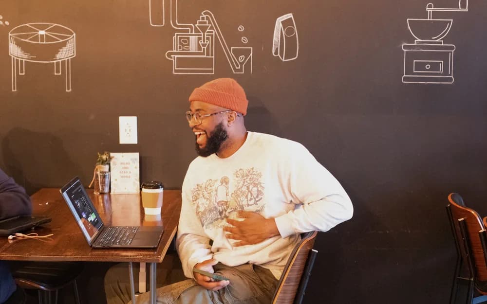 A builder laughing mid-conversation beside an open laptop at SheBuilds
